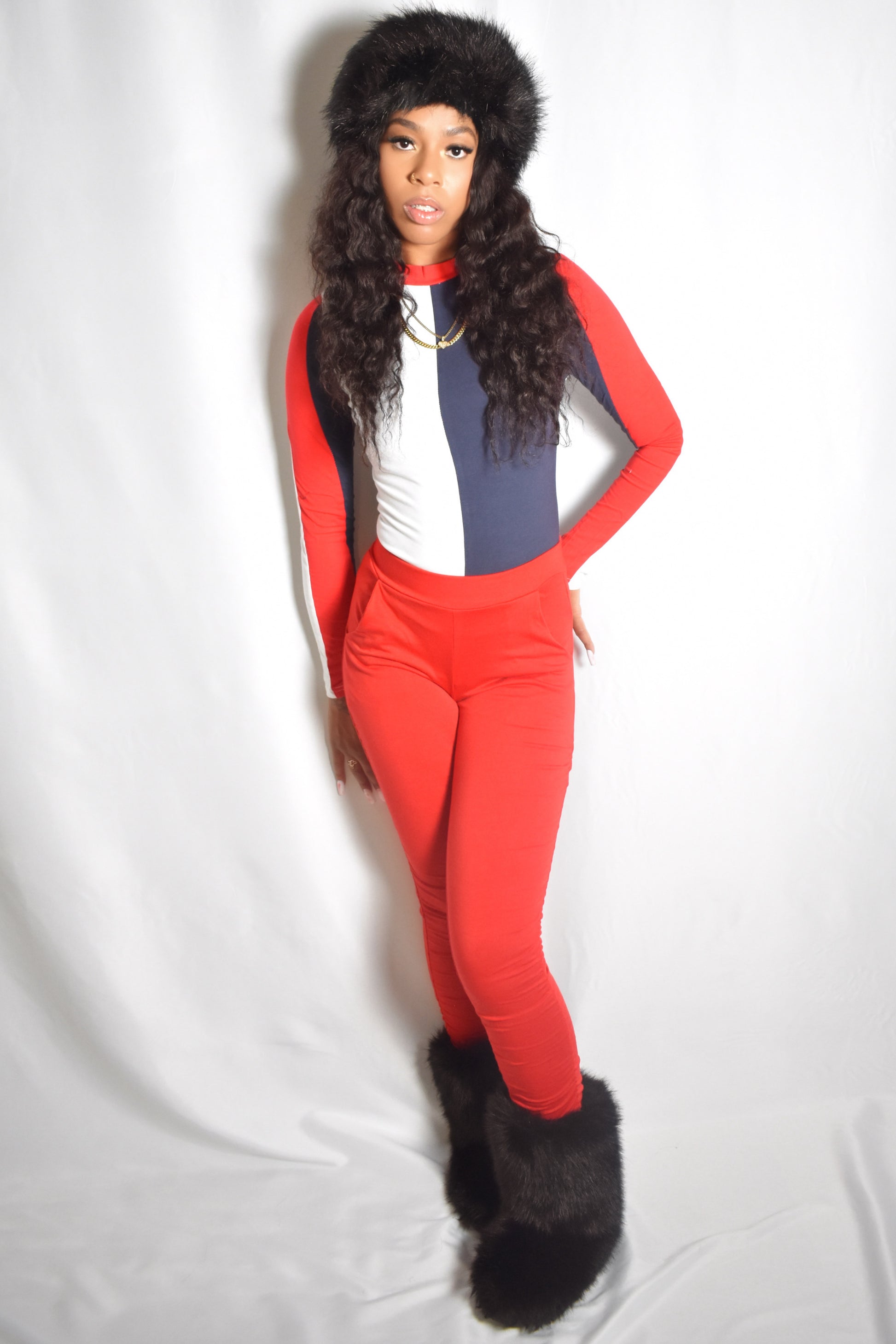 Arctic Rebel color block bodysuit in red, white, and blue with slim fit. Red stacked pants. Black jumbo faux fur headband and boot accents.