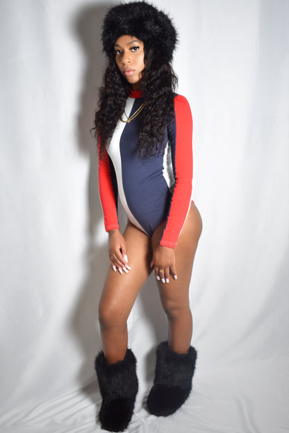 Person wearing a blue and red bodysuit with black fur headband and boots on a white background. Arctic Rebel color block bodysuit in red, white, and blue with slim fit. Red stacked pants. Black jumbo faux fur headband and boot accents.