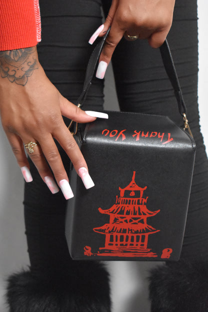 black bag with red pagoda design held by a person wearing a red outfit. Kawaii Kiss Asian takeout-style bag with tower illustration and ‘Thank You’ text.
