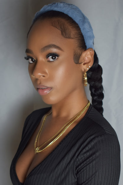 Woman with braided hair wearing a blue headband and gold jewelry. Snow Crown faux fur headband in soft plush material. Close-up of Snow Crown faux fur texture. Side view of furry Snow Crown headband with cozy fit. Snow Crown faux fur headband styled as cute Y2K winter accessory. Snow Crown faux fur headband available in multiple colors.