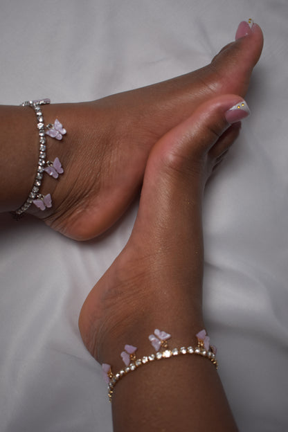 Close-up of a foot with butterfly-themed anklets on a white background. Feet wearing anklets with butterfly charms on a white background. Purple butterfly anklet detail. Y2K anklet with purple butterfly accents. Luxury ankle jewelry with butterfly charm. Purple butterfly anklet styled on ankle