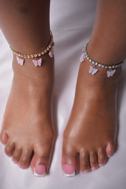 Feet wearing anklets with butterfly charms on a white background. Pink Purple butterfly anklet detail. Y2K anklet with pink purple butterfly accents. Luxury ankle jewelry with butterfly charm. pink Purple butterfly anklet styled on ankle