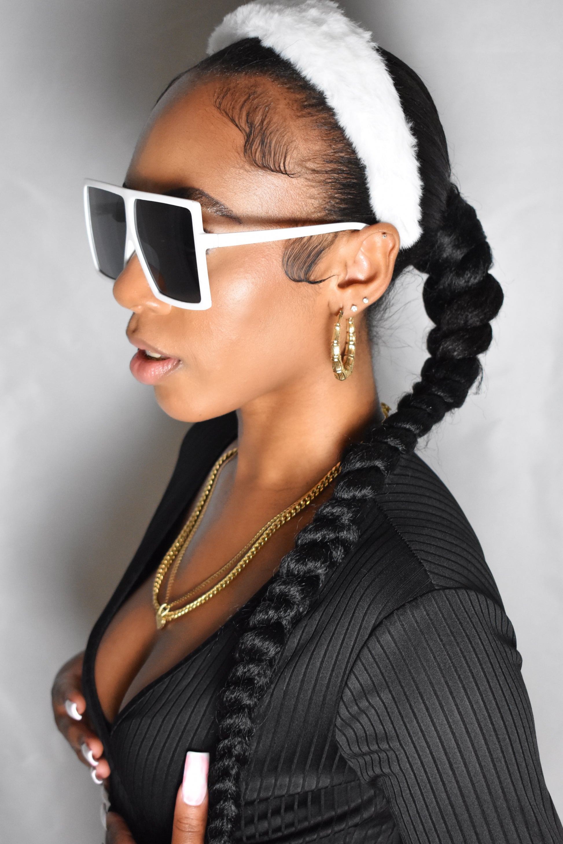 Woman with braided hair wearing a blue headband and gold jewelry. Snow Crown faux fur headband in soft plush material. Close-up of Snow Crown faux fur texture. Side view of furry Snow Crown headband with cozy fit. Snow Crown faux fur headband styled as cute Y2K winter accessory. Snow Crown faux fur headband available in multiple colors. White extra iconic sunglasses.