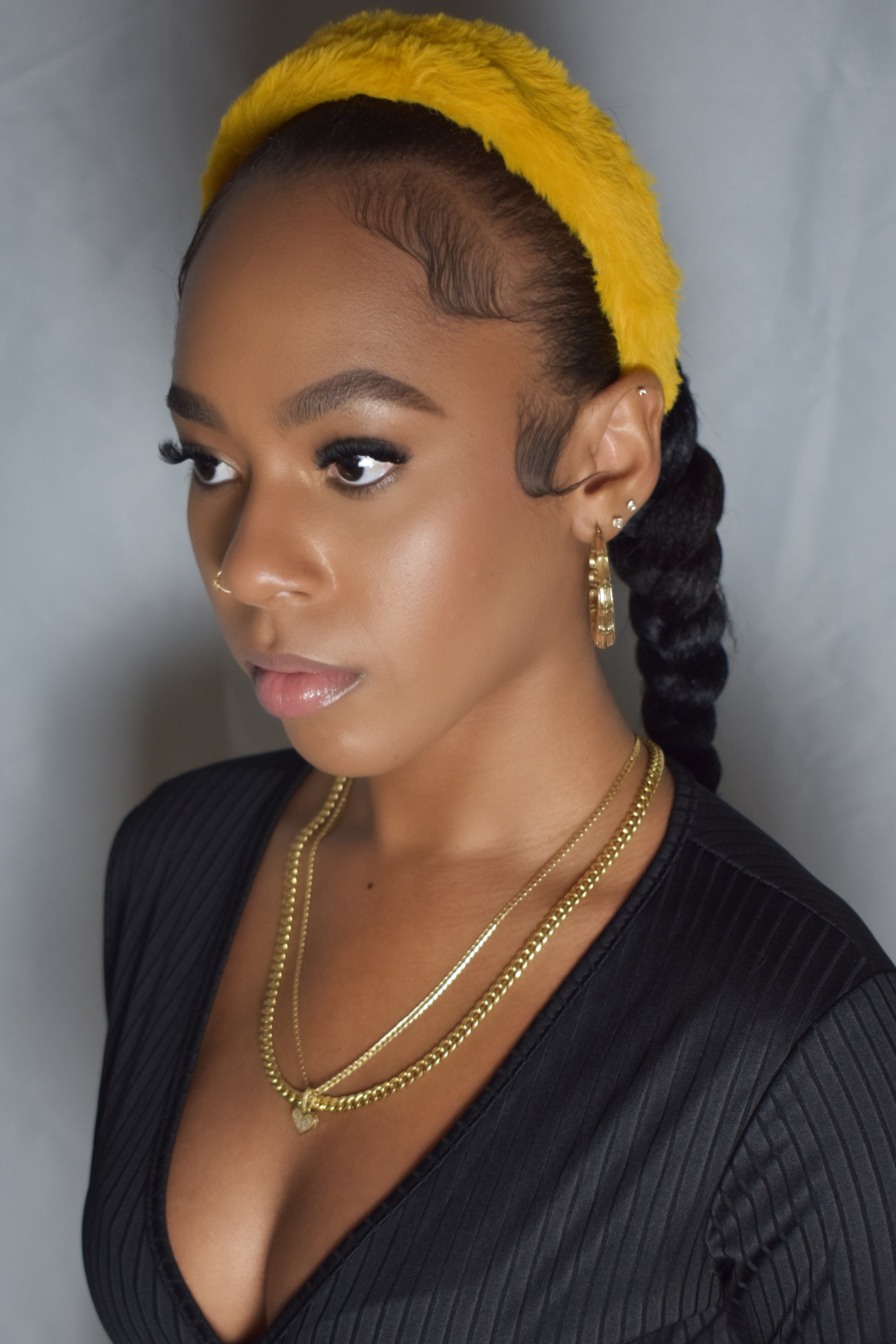 Woman with braided hair wearing a blue headband and gold jewelry. Snow Crown faux fur headband in soft plush material. Close-up of Snow Crown faux fur texture. Side view of furry Snow Crown headband with cozy fit. Snow Crown faux fur headband styled as cute Y2K winter accessory. Snow Crown faux fur headband available in multiple colors.