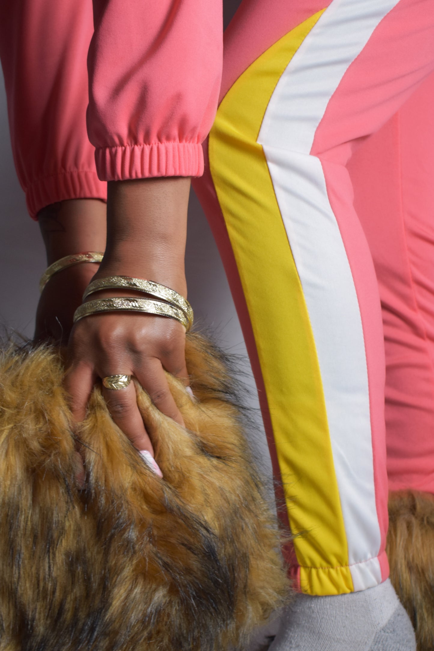 Person wearing a colorful jacket with pink, yellow, and gray stripes, holding a fur boot. pink retro y2k tracksuit color block with yellow and white accents, brown faux fur boots, brown jumbo faux fur headband, two piece outfit set