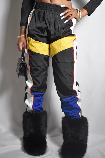 front view of raw retro color block black track pants with yellow, white and blue accents, black fur boots, mini leather handbag, with vintage y2k design