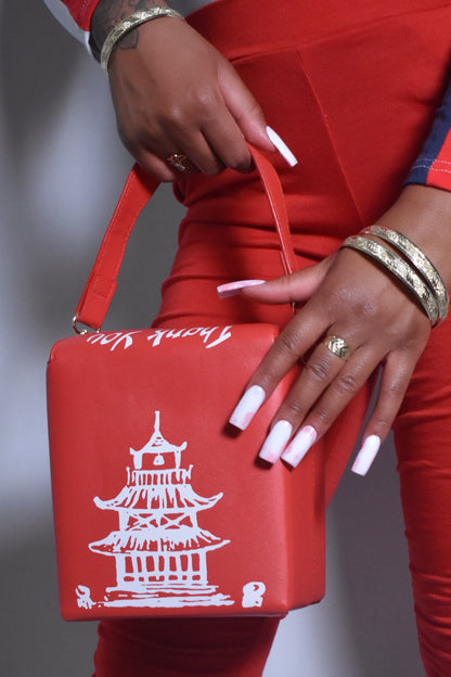 Red bag with white pagoda design held by a person wearing red pants and gold jewelry. Kawaii Kiss Asian takeout-style bag with tower illustration and ‘Thank You’ text.
