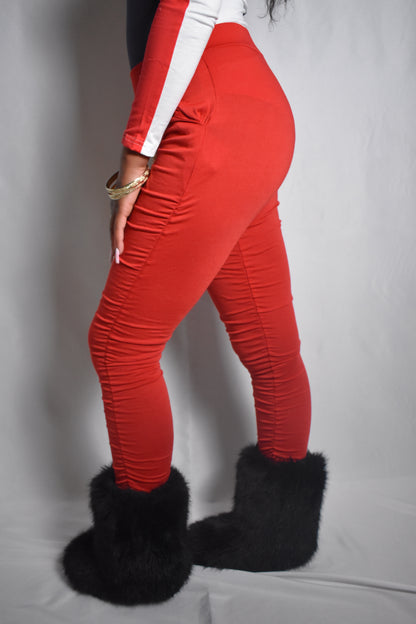 Model wearing red stacked pants with fitted silhouette. Black faux fur boots. Red handbag