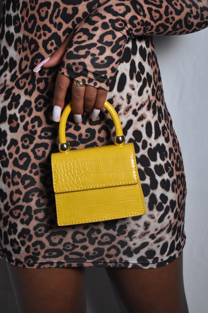 leopard print outfit holding a mustard yellow handbag. Mustard yellow crocodile-patterned handbag with gold accents. Essentials Only mini faux leather handbag in yellow mustard, compact and chic design. textured faux leather and structured silhouette. sleek faux leather finish